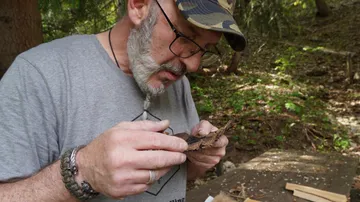 Mann untersucht Holzstück in einem Wald.