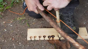 A person rubs a stick on wood to make a fire.