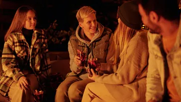 Four people sit around the campfire and enjoy drinks.