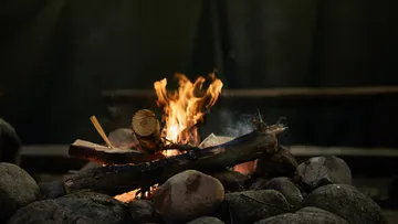 Fire burns on wood surrounded by large stones.