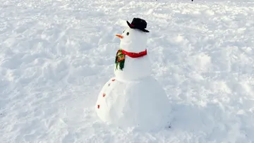 Snowman stands in fresh, untouched snow, decorated.
