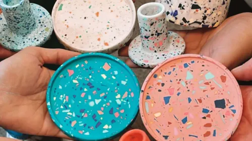 Colourful, terrazzo-like objects are held by hands.