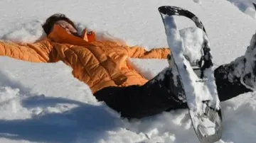 Person liegt im Schnee und spielt mit Schneeschuhen.