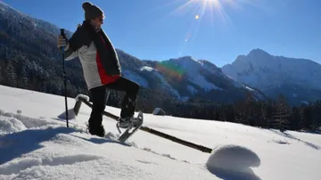 Junger Mensch wandert mit Schneeschuhen im verschneiten Gebirge.