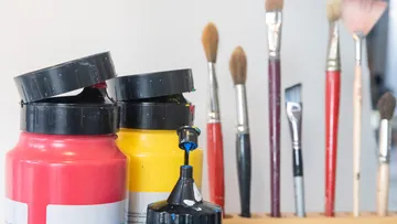 Paint pots stand next to brushes against a neutral background.