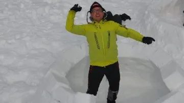 Mann in gelber Jacke springt fröhlich im Schnee.