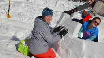 Menschen bauen einen Schneehaufen im sonnigen, verschneiten Gelände.