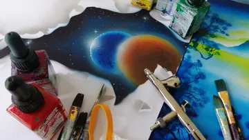 Paints and brushes surround a planetary painting.