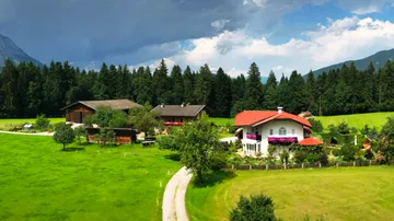 Landschaft mit Bauernhäusern, umgeben von Bäumen und Wiesen.