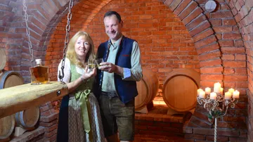 Paar hält Gläser in einem Keller mit Holzfässern.