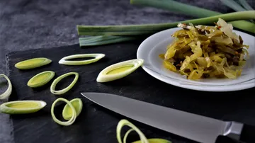 Pieces of leek lie next to a plate of pickled vegetables.