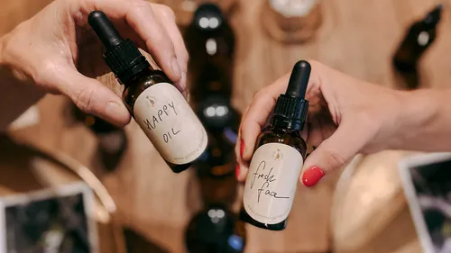 Two hands hold bottles of oils, the background is wood.