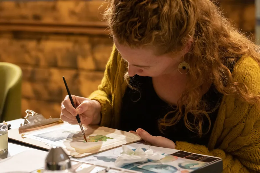 A person concentrates on a canvas at the table.