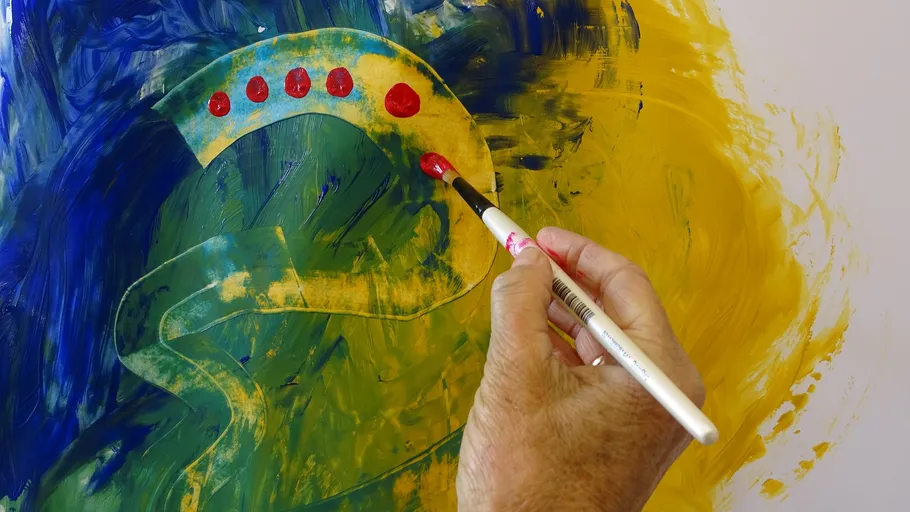 A hand paints red dots on a colorful canvas.