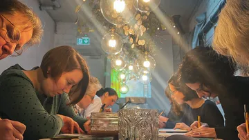 Gruppendiskussion, Teilnehmer zeichnen, gemütliche Café-Atmosphäre.