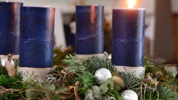 Dunkelblaue Kerzen brennen auf einem festlichen Adventskranz.