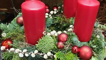 Rote Kerzen stehen zwischen grünen Zweigen und roten Kugeln.