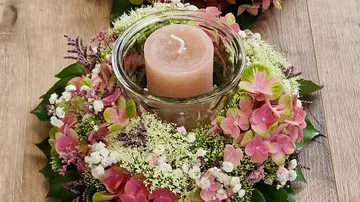 A candle stands in a floral, decorative arrangement.