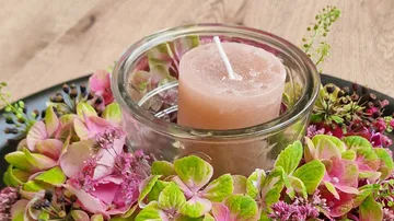 A candle stands in the midst of colorful flower arrangements.