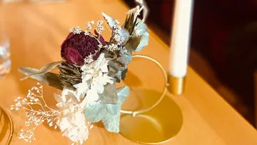 Trockenblumen arrangiert in einem goldenen Halter auf Tisch.