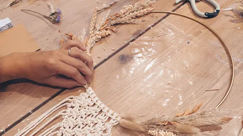 Hand is working on a decoration made from dried flowers and yarn.