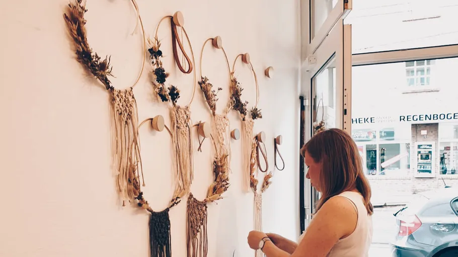 Wreaths of flowers hang on the wall; a woman is working on them.