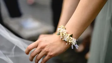 Ein Arm mit einem Blumenarmband hält einen Schleier.
