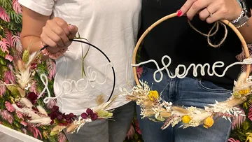 Two women hold decorative wreaths with lettering.