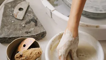 Hand molds clay in a bowl on a table.
