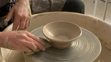 Hands form a clay bowl in a potter's wheel.