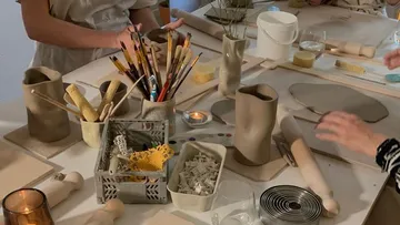 Tisch mit Töpfermaterialien, Hände formen Keramikobjekte.