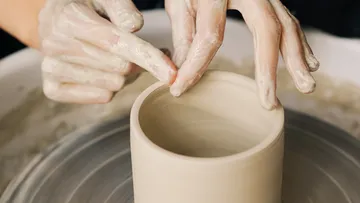 Hands form a clay cup on a turntable.