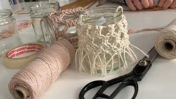 Glas mit Makramee-Verzierung auf einem Tisch, umgeben von Materialien.