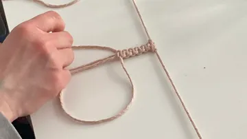 Eine Hand knüpft einen Knoten mit einer Schnur auf einem Tisch.
