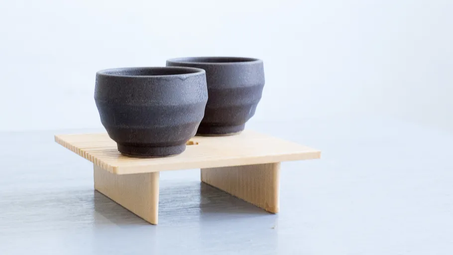 Two cups stand on a wooden stand.