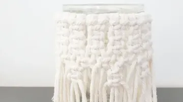 Glass vase with white macrame coating is on the table.