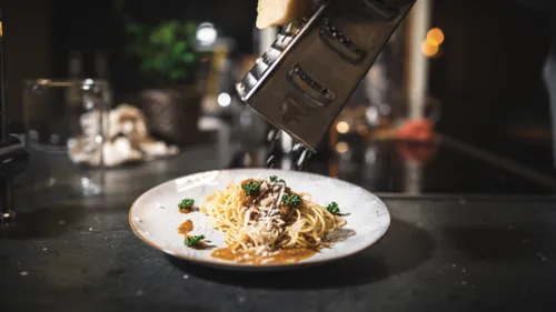 Grating cheese over spaghetti dish in kitchen.