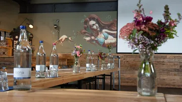 Vase mit Blumen auf Tisch, Wandgemälde im Hintergrund.