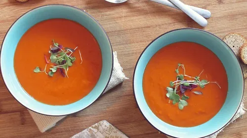 Zwei Schalen Tomatensuppe mit frischen Kräutern, auf Holzuntergrund.