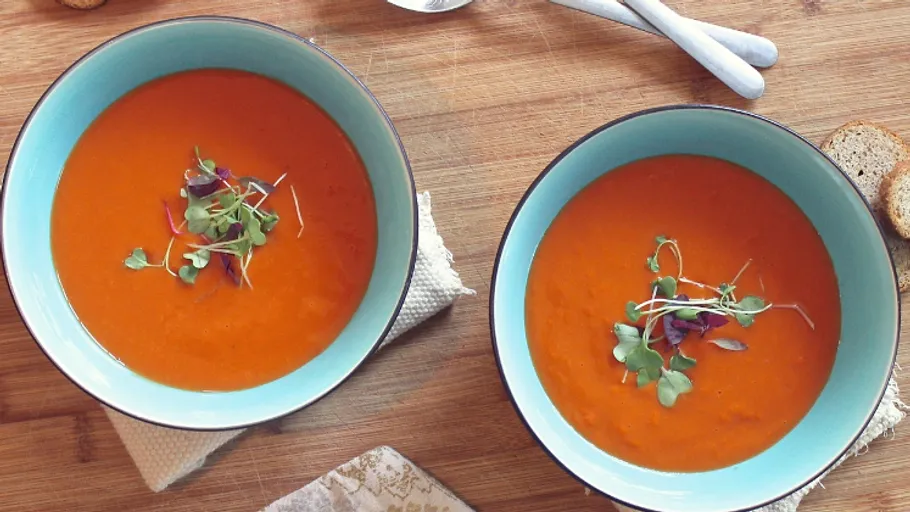 Zwei Schalen Tomatensuppe mit frischen Kräutern, auf Holzuntergrund.