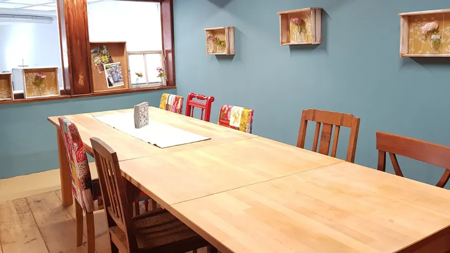 Holztisch im Raum, umgeben von bunten Stühlen.