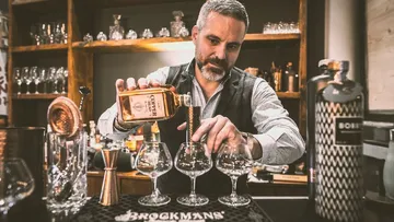 Bartender gießt Getränk in Gläser an einer Bar.