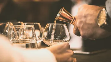 Ein Glas wird mit Flüssigkeit von einem Messbecher gefüllt.