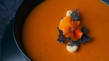 Suppe in schwarzem Schüssel, garniert mit Blüten und Chips.