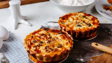 Törtchen aus Teig mit Käse und Gemüse auf Holzunterlage.