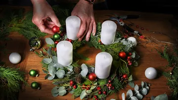 Hands decorate an Advent wreath with candles and Christmas tree balls.