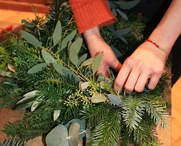 Hands make a wreath from green plant branches.