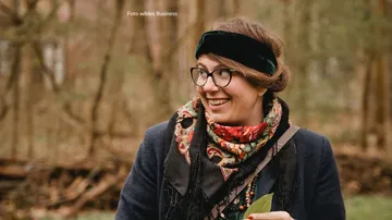 Frau lächelt, hält Blatt, im Waldumfeld.