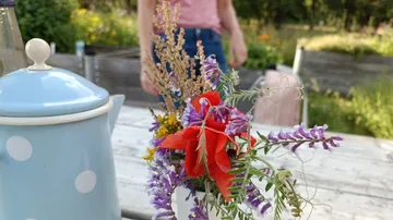 Blauer Teekanne neben buntem Blumenstrauß auf Tisch im Garten.