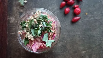 Glas mit getrockneten Kräutern und Blüten, auf Holzuntergrund.